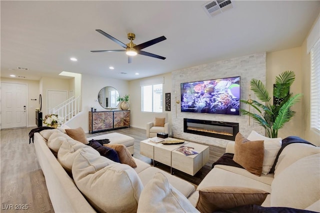 living area with visible vents, wood finished floors, stairs, ceiling fan, and a fireplace