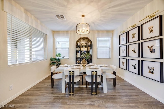 dining area featuring visible vents, wood finished floors, baseboards, and an inviting chandelier