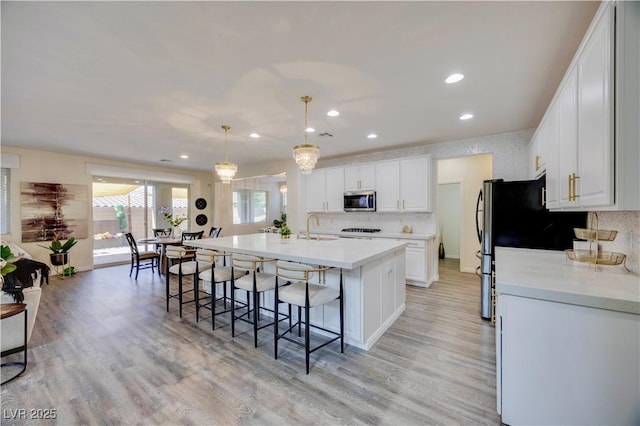 kitchen with recessed lighting, an island with sink, stainless steel appliances, a kitchen bar, and white cabinetry