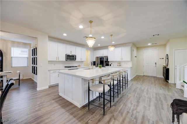 kitchen featuring light wood finished floors, visible vents, white cabinetry, decorative backsplash, and appliances with stainless steel finishes