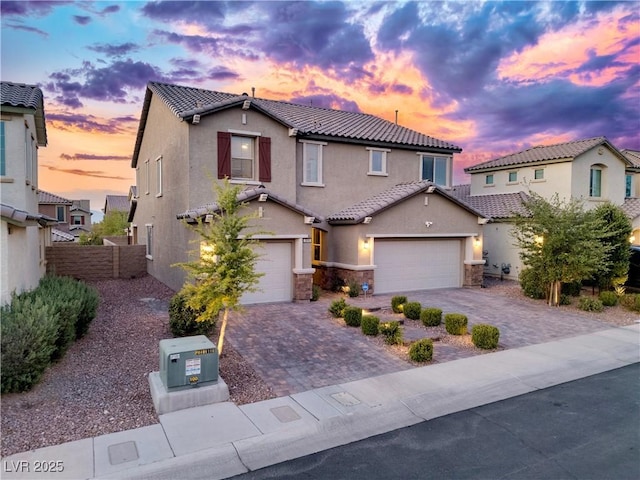 traditional-style home featuring a tile roof, stone siding, fence, stucco siding, and decorative driveway