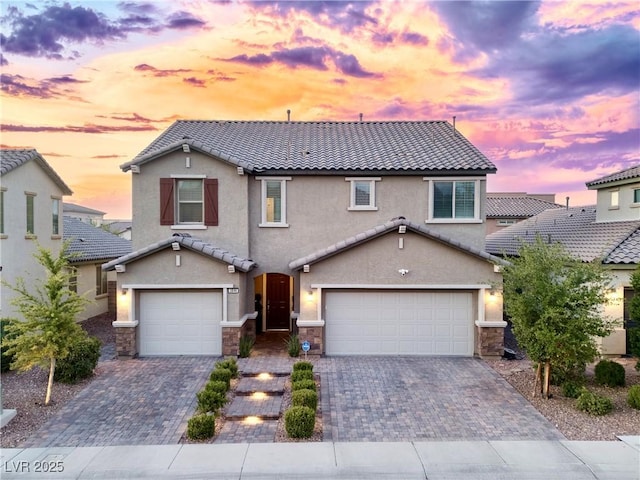 traditional-style house with a tile roof, decorative driveway, stone siding, and a garage