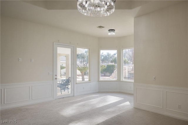 empty room featuring a chandelier, a decorative wall, visible vents, and carpet flooring