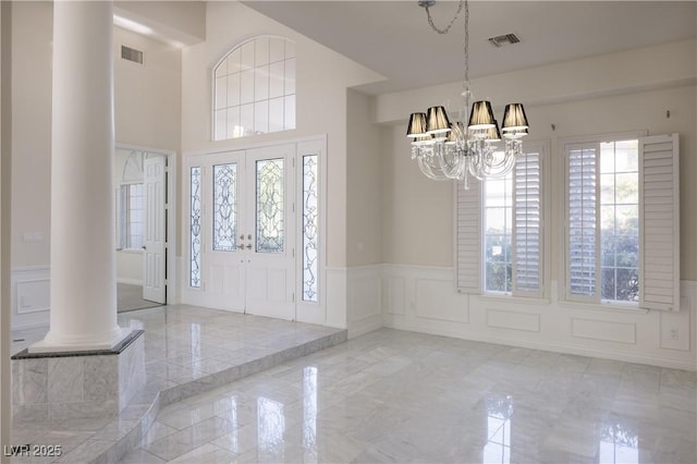 entrance foyer featuring a decorative wall, visible vents, marble finish floor, and ornate columns