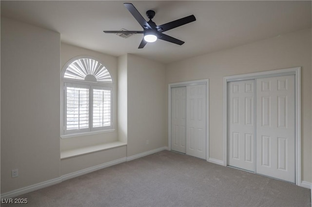 unfurnished bedroom with multiple closets, carpet flooring, baseboards, and ceiling fan