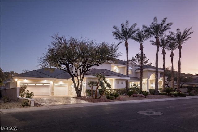 view of front facade featuring a garage, a tile roof, stucco siding, and driveway