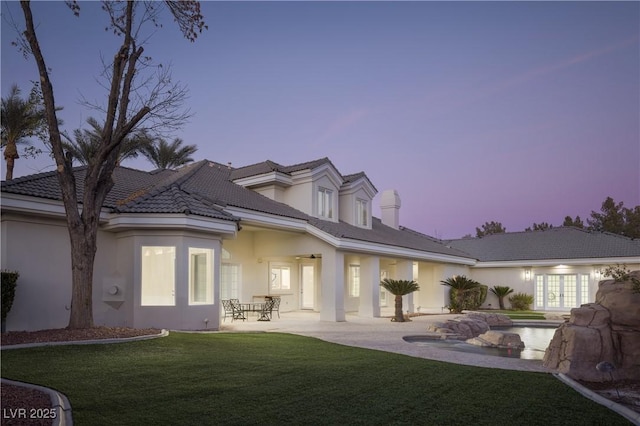 rear view of house with a patio area, a lawn, an outdoor pool, french doors, and stucco siding
