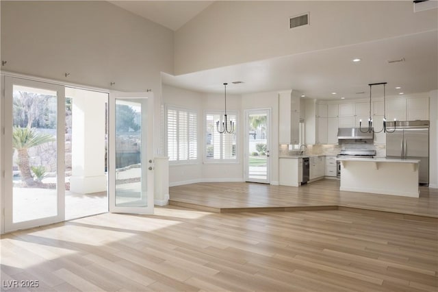 unfurnished living room with visible vents, a sink, light wood-type flooring, baseboards, and a notable chandelier