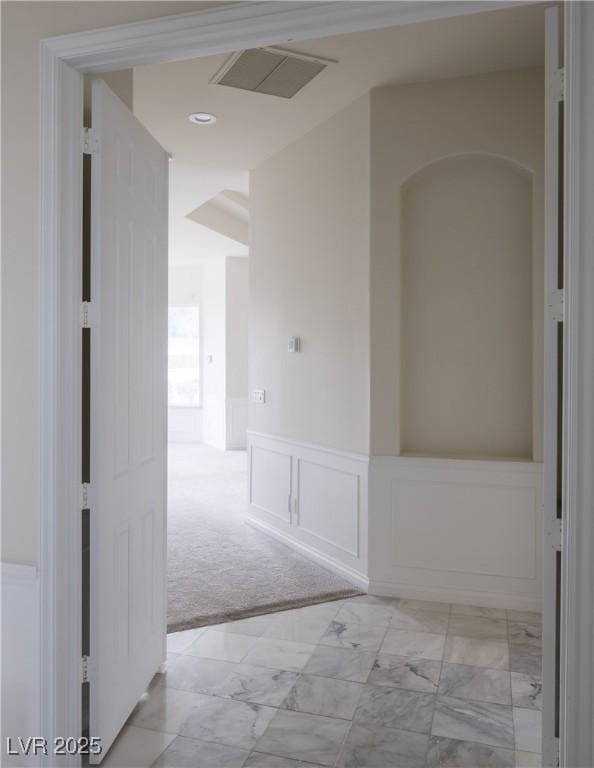 hallway with marble finish floor, a wainscoted wall, visible vents, a decorative wall, and light colored carpet