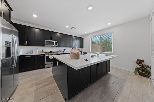 31 Strada Loreto, Henderson, NV 89011 - kitchen with a kitchen island with sink, stainless steel appliances, light countertops, dark cabinets, and visible vents