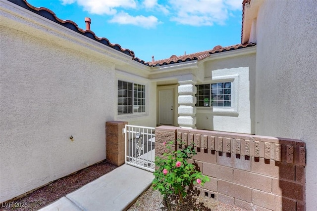 property entrance with a tiled roof, a gate, and stucco siding