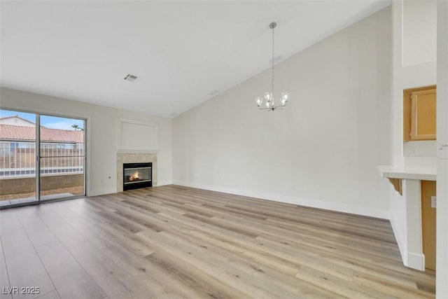 unfurnished living room featuring light wood-style floors, a tile fireplace, high vaulted ceiling, and a notable chandelier