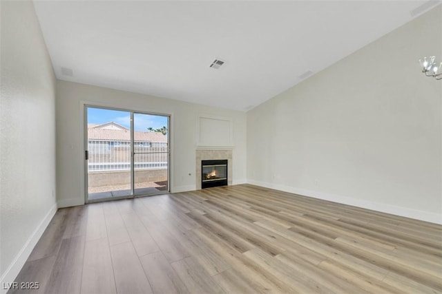 unfurnished living room featuring a tile fireplace, an inviting chandelier, visible vents, light wood-style floors, and baseboards