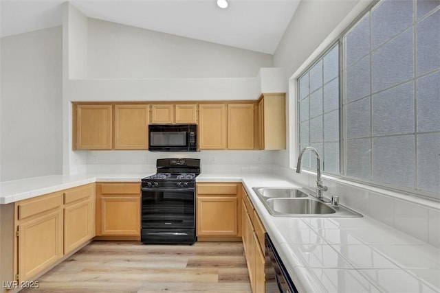 kitchen featuring light brown cabinets, a sink, light wood-style floors, and black appliances