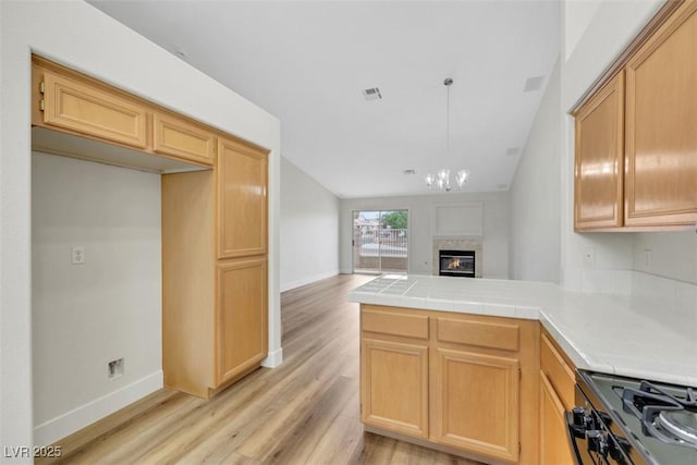 kitchen featuring tile counters, light wood-type flooring, a peninsula, baseboards, and visible vents