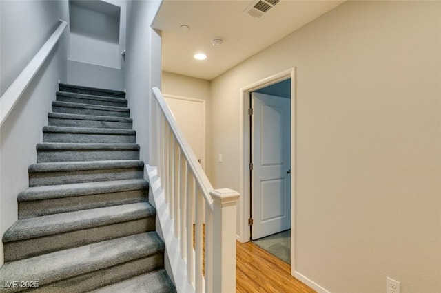 staircase with wood finished floors, baseboards, and recessed lighting