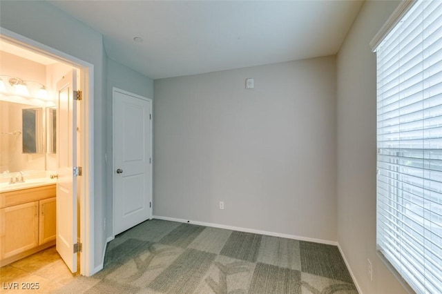 unfurnished bedroom featuring light colored carpet, multiple windows, baseboards, and ensuite bathroom