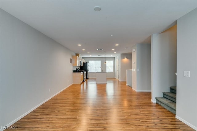 unfurnished living room with light wood-style floors, recessed lighting, stairs, baseboards, and a sink