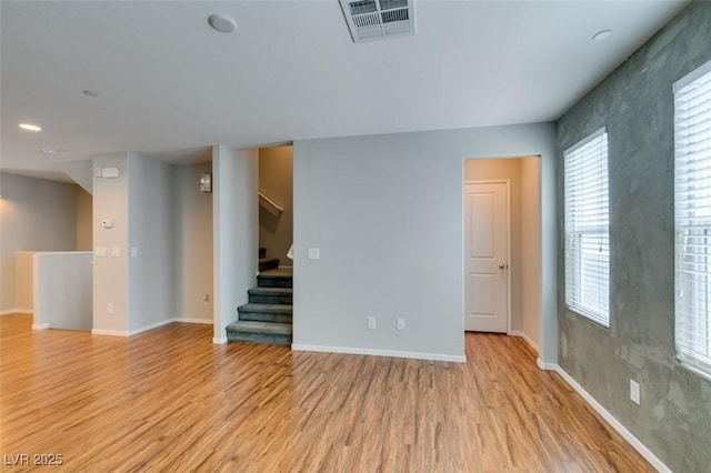 spare room featuring light wood finished floors, baseboards, and stairs