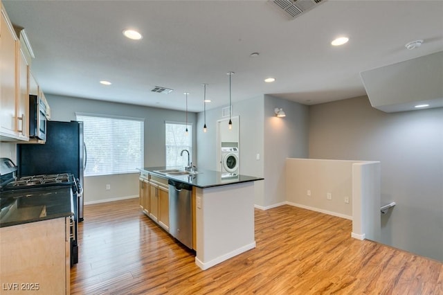 kitchen featuring washer / dryer, appliances with stainless steel finishes, a sink, dark countertops, and light wood-type flooring