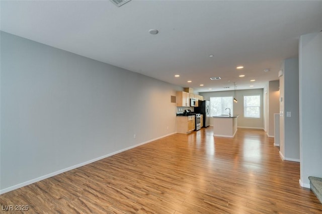 unfurnished living room featuring light wood-style floors, baseboards, recessed lighting, and a sink
