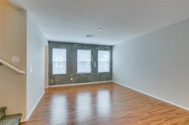 empty room featuring wood finished floors, baseboards, and stairway