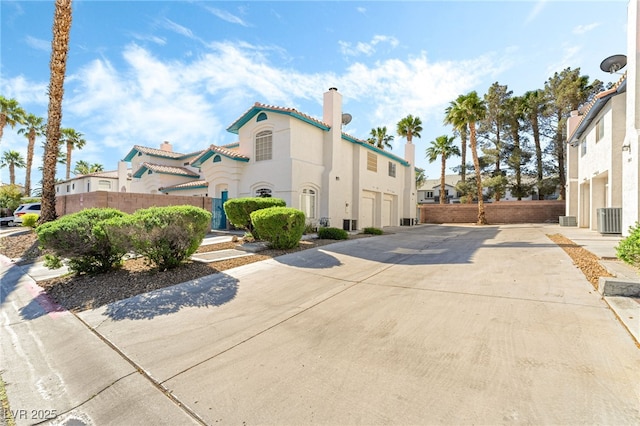 view of home's exterior featuring concrete driveway, a chimney, stucco siding, cooling unit, and fence