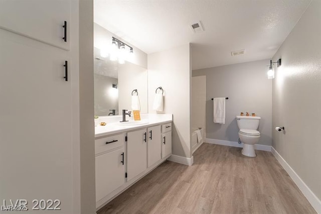 bathroom with wood finished floors, vanity, baseboards, toilet, and visible vents