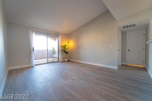 spare room featuring vaulted ceiling, wood finished floors, visible vents, and baseboards