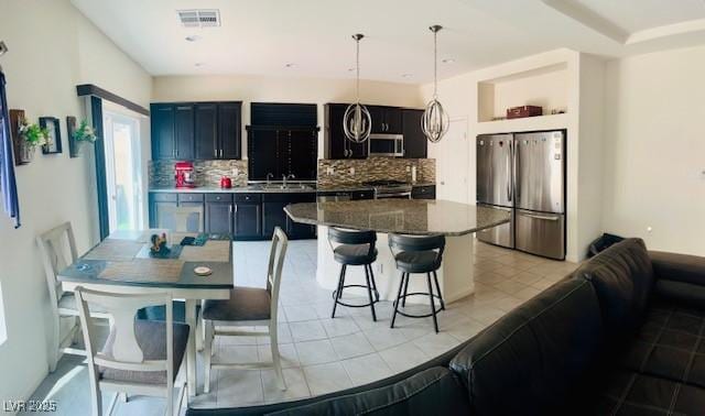 kitchen featuring a sink, a kitchen breakfast bar, visible vents, decorative backsplash, and appliances with stainless steel finishes