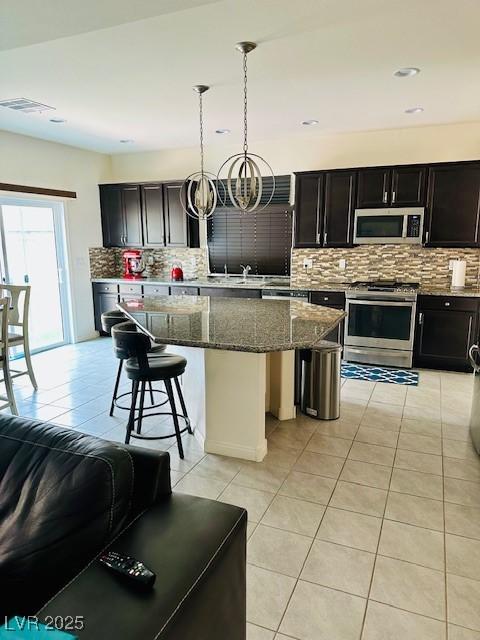 kitchen with dark stone countertops, decorative backsplash, light tile patterned floors, a kitchen island, and appliances with stainless steel finishes