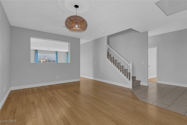 unfurnished living room featuring baseboards, wood finished floors, and stairs