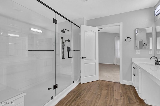 full bath featuring baseboards, vanity, wood finished floors, and a stall shower