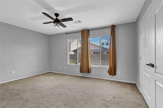carpeted empty room with baseboards, a ceiling fan, and visible vents