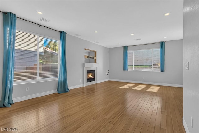 unfurnished living room with a fireplace, wood finished floors, visible vents, and baseboards