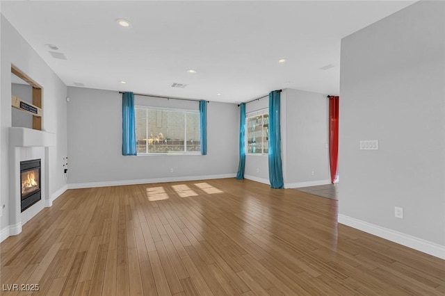 unfurnished living room with baseboards, wood finished floors, a glass covered fireplace, and recessed lighting