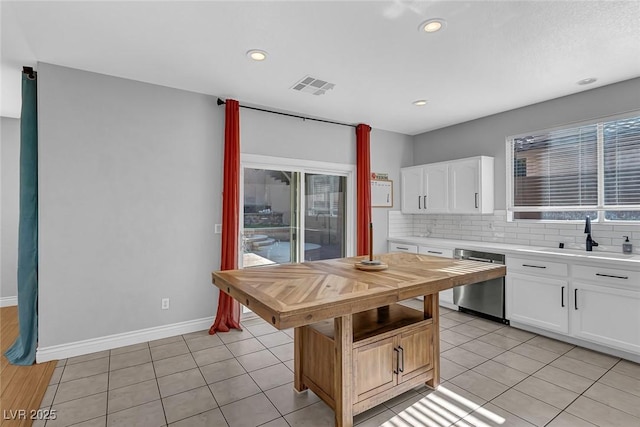 kitchen with stainless steel dishwasher, a sink, wooden counters, white cabinetry, and visible vents