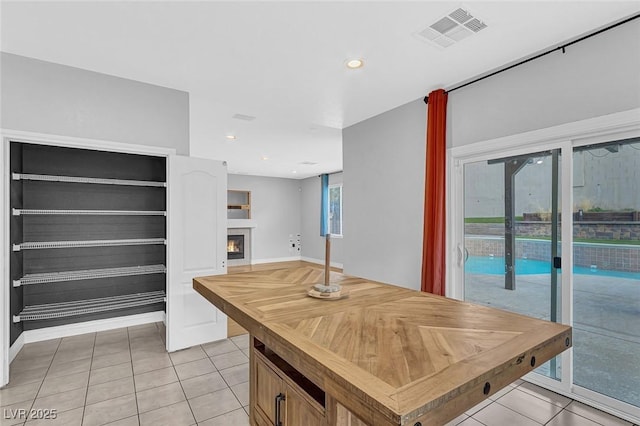 kitchen with a warm lit fireplace, light tile patterned flooring, butcher block counters, visible vents, and recessed lighting