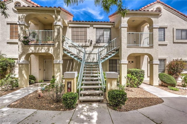 view of front of property featuring stucco siding, stairway, a balcony, and a tile roof