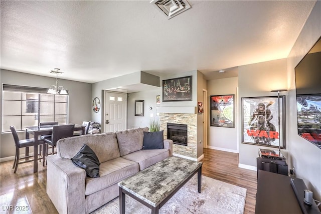 living area featuring a chandelier, visible vents, baseboards, a fireplace, and wood finished floors