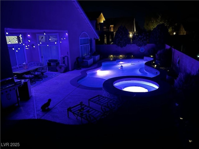 pool at night featuring a patio area, a pool with connected hot tub, and a fenced backyard