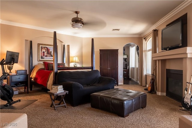 carpeted living room with visible vents, ornamental molding, arched walkways, baseboards, and a glass covered fireplace