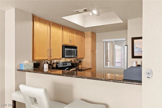 220 E Flamingo Rd Unit 111, Las Vegas, NV 89169 - kitchen featuring stainless steel appliances, light brown cabinetry, dark stone countertops, a textured wall, and a tray ceiling