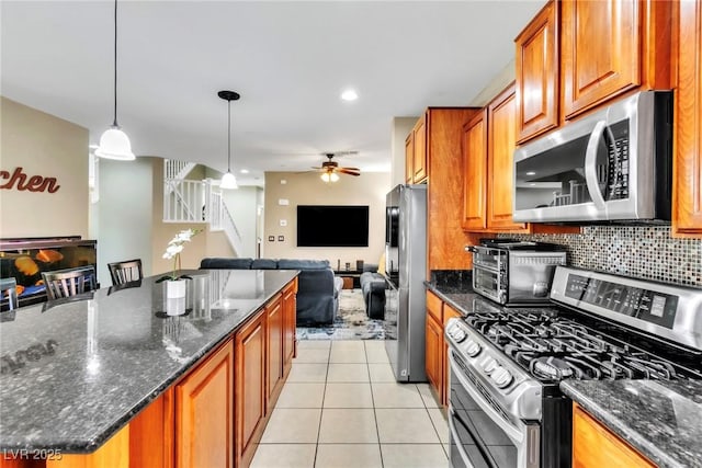 kitchen featuring appliances with stainless steel finishes, open floor plan, ceiling fan, brown cabinetry, and decorative backsplash