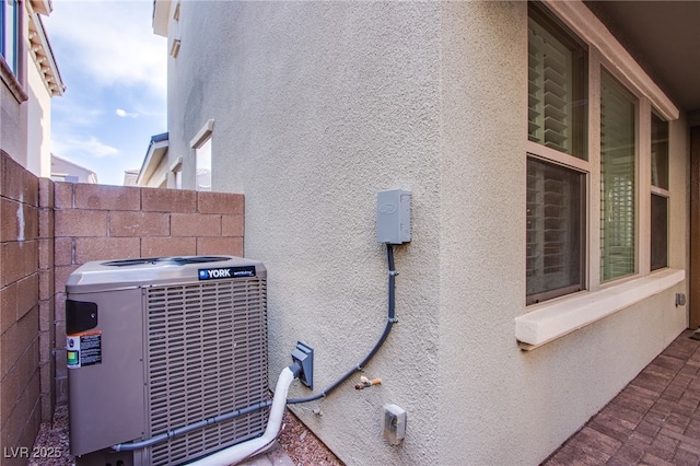 view of side of property featuring fence, central AC, and stucco siding