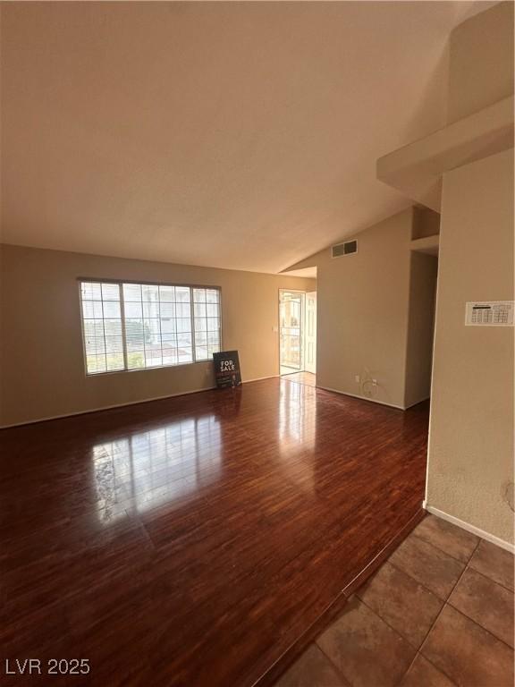 unfurnished room with dark tile patterned floors, lofted ceiling, visible vents, and baseboards