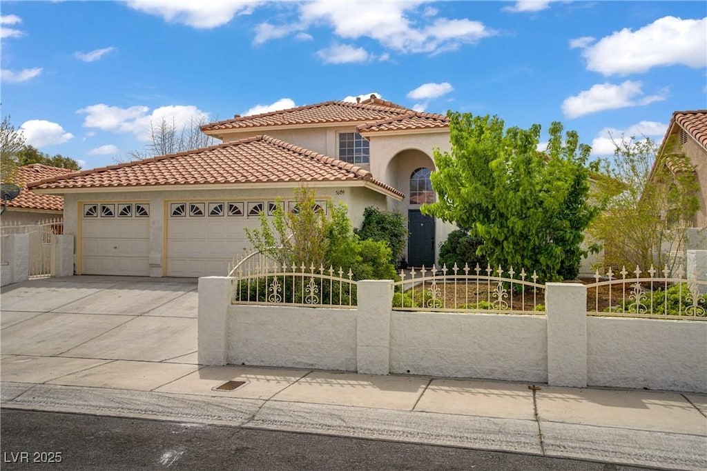 mediterranean / spanish house with a garage, a tile roof, driveway, and a fenced front yard