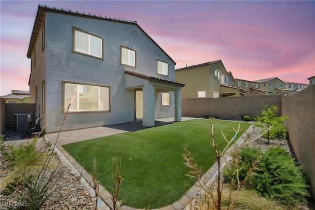 back of house at dusk featuring a lawn, a patio, a fenced backyard, and stucco siding