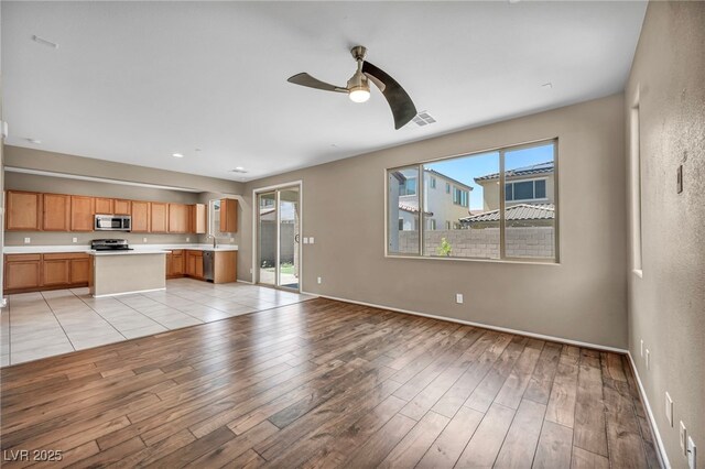 unfurnished living room with baseboards, light wood-style flooring, visible vents, and a ceiling fan