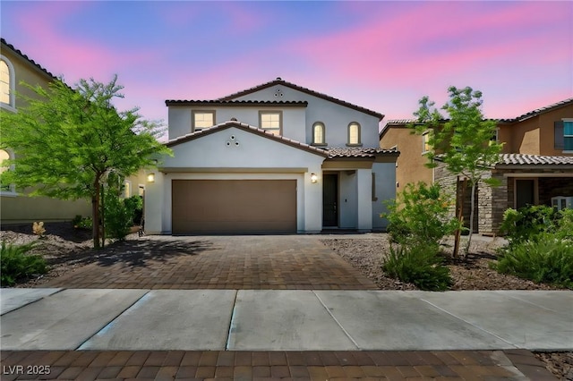 mediterranean / spanish house featuring a garage, stucco siding, a tile roof, and decorative driveway